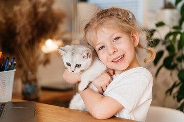 child playing with little cat. A little girl holds a white kitten. A little girl snuggles up to a cute pet and smiles while sitting in the living room of the house. Happy Children and pets.