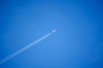 looking up at an Easyjet Airbus A320 twin engine jet airliner in deep blue sky with vapour trails diagonally across the frame