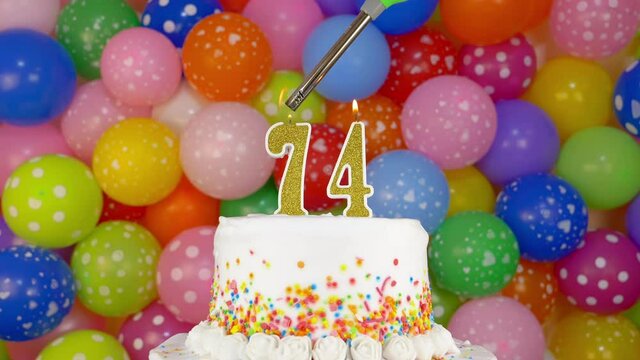 Cake with burning candles number 74. A tasty celebration cake on a bright festive background of colorful balloons.