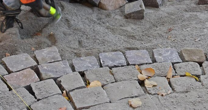 The road master in gloves lays paving stones in layers stone road by professional paver worker