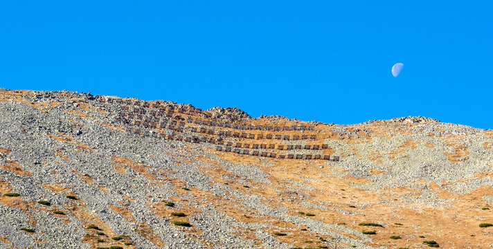 Avalanche protection or barrier on Lomnicke sedlo mountain pass in High Tatras with moon in the blue sky. Slovakia.