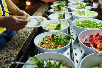 Male hands holding  a plate and taking food at the restaurant with fresh and organic salads. Self-service food in a mall.  Salad meals on counter top at buffet catering service 