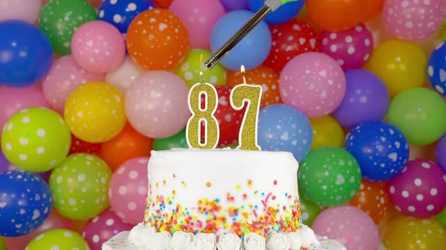 Cake with burning candles number 87. A tasty celebration cake on a bright festive background of colorful balloons.