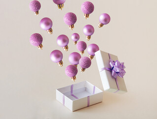 Christmas baubles flying out from the gift box. Purple aesthetic New Year creative concept. Beige background.