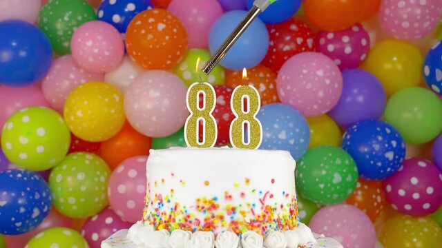 Cake with burning candles number 88. A tasty celebration cake on a bright festive background of colorful balloons.
