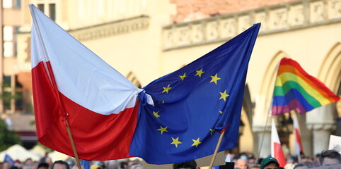 flags of the european union nad Poland tied together on street pro UE demonstration, in background rainbow flag holds by demonstrators