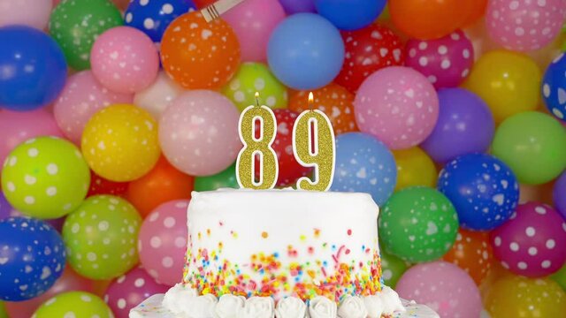 Cake with burning candles number 89. A tasty celebration cake on a bright festive background of colorful balloons.
