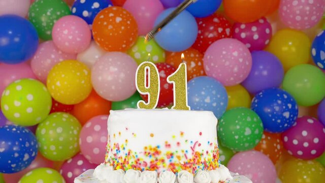 Cake with burning candle number 91. A tasty Birthday Cake on a bright festive background of colorful balloons.