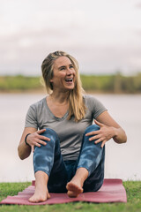 Happy blonde woman sitting on a yoga mat outdoors