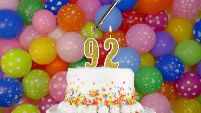 Cake with burning candle number 92. A tasty Birthday Cake on a bright festive background of colorful balloons.