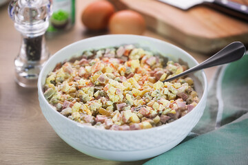 Large bowl of Russian traditional salad olivier with pea on wooden background