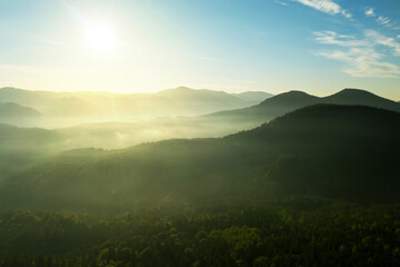 Sun shining over forest in misty mountains. Drone photography