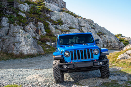 St. John's, Newfoundland, Canada, December 2021: A vibrant blue Jeep Gladiator Rubicon truck 4x4 off-road and parked on the side of a hill with the blue ocean, blue sky, and clouds in the background. 
