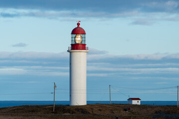 The watch room of a lighthouse.The lantern room has a large green bulb. The building is white with a red rail around the gallery deck.The background is cloudy and there's vignetting around the edges. 