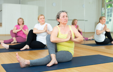 Fototapeta na wymiar Women exercising during yoga class in modern fitness center - marichiasana pose