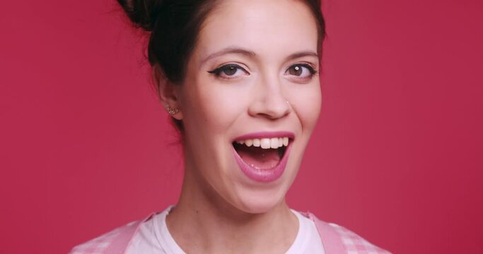 Close up of Smiling beautiful young woman in pink clothes posing isolated on pink background in studio. People sincere emotions lifestyle concept Looking into camera charming smile wink blink eye