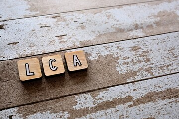 The letters arranged in the word LCA It's an abbreviation for Life Cycle Assessment. It's on a wihte wooden board.