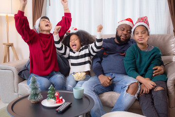 Happiness African family watching movie with excited and fun in the living room for leisure with comfort at home on Christmas day, dad and mom and daughter cheering watching tv with victory.