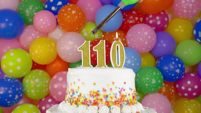 Cake with burning candles number 110. A tasty Birthday Cake on a bright festive background of colorful balloons.
