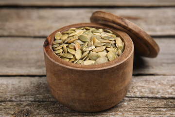 Dish with pumpkin seeds and lid on wooden table, closeup