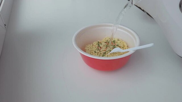 A man pours boiling water into instant noodles. Cooking instant noodles.