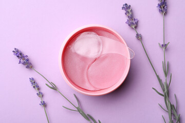 Under eye patches in jar with spatula and lavender flowers on lilac background, flat lay. Cosmetic product