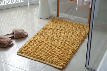Soft orange bath mat and slippers on floor indoors