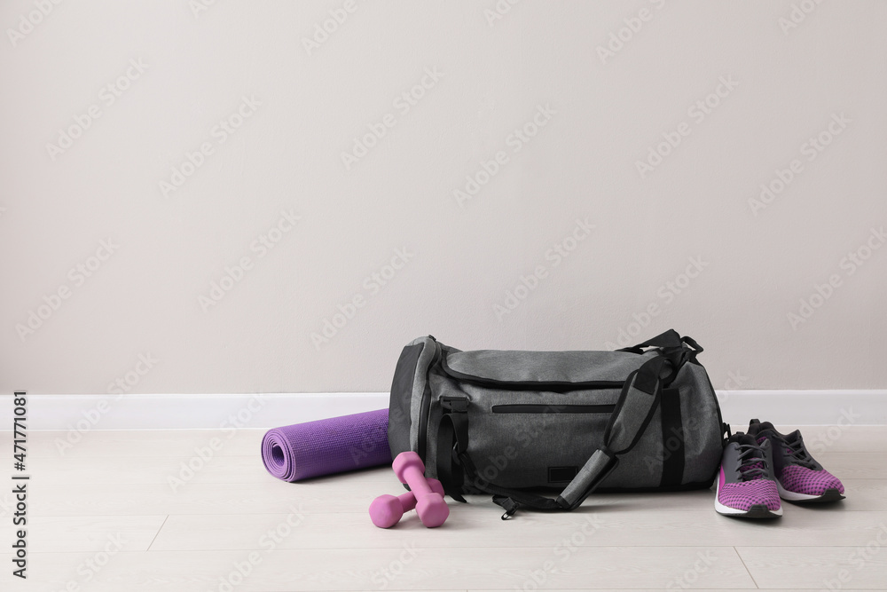 Sticker Grey bag and sports accessories on floor near light wall, space for text