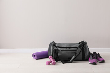 Grey bag and sports accessories on floor near light wall, space for text
