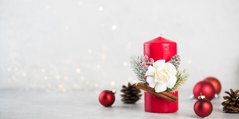  Christmas red candle surrounded by Christmas balls, cones on a light background with bokeh. Banner. Copy space.