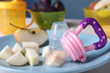 Nibbler with fresh apple on light blue plate, closeup. Baby feeder