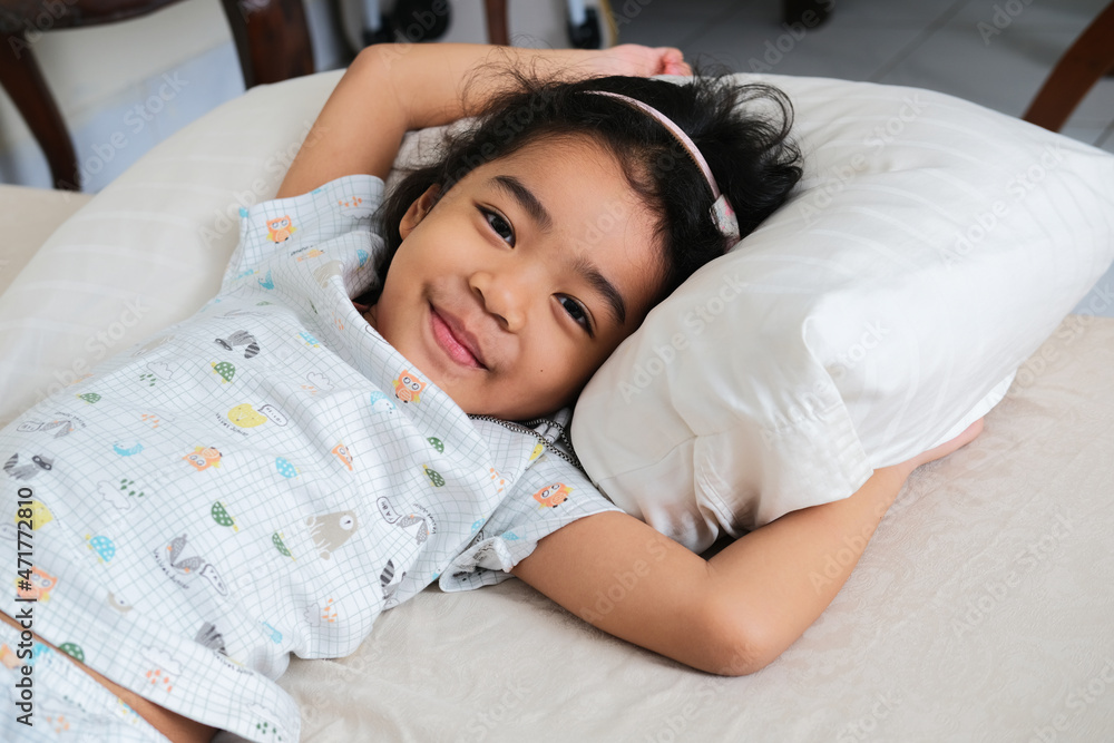 Wall mural Asian little girl smiling happy in her bed after wake up in the morning