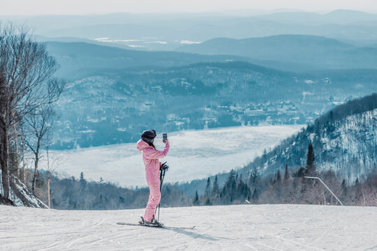 Woman taking photo on ski vacation using phone - Woman skier using phone app on ski trail slope taking pictures of amazing winter nature landscape. Girl using mobile smartphone in awesome ski wear