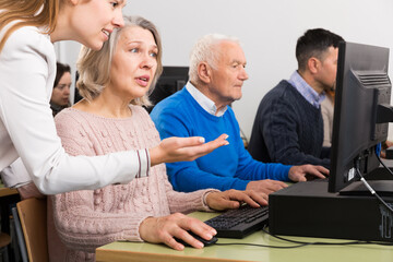 Side view of young business woman explaining something to older coworkers, pointing at computer monitor