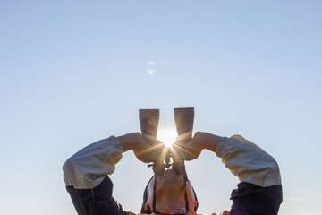 Young male man holding binoculars looking sky at beautiful sunset background.