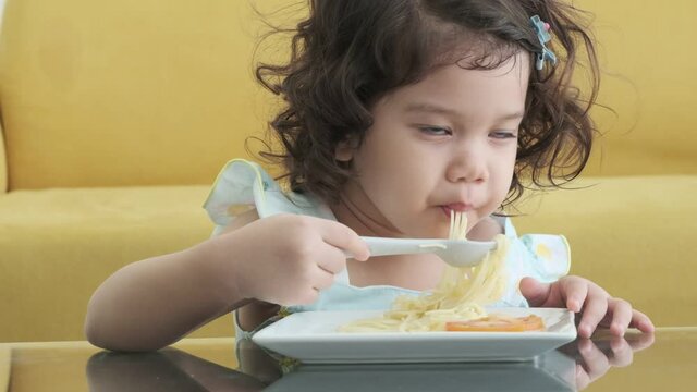 Cute girl eats pasta noodles sitting in room,slow motion shot.