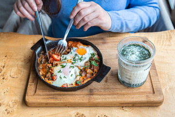 Close-up, a woman in a cafe dines on traditional shakshuka.