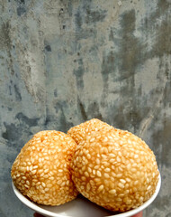 Three fried sesame balls with mung beans filling, called onde-onde in Indonesia, placed in a white small plate.
