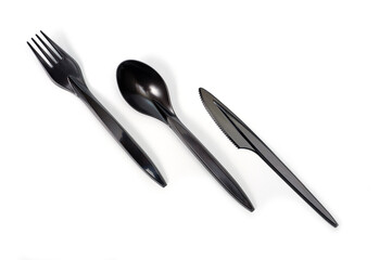 A set of plastic cutlery knife, fork and spoon in black, filmed on a white background