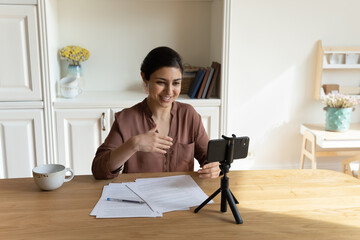 Smiling beautiful young indian woman recording educational video on cellphone web camera, sharing...