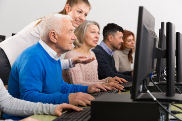 Positive young female coach giving computer lessons for group of middle aged people ..