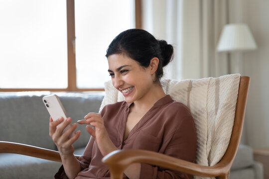 Happy young indian woman laughing looking at smartphone screen, reading message with good news, enjoying pleasant communication in social network, using e-dating application, playing online game.