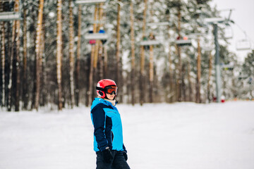 Fototapeta na wymiar a girl in a helmet and mask stands on a ski slope in a snow-covered forest