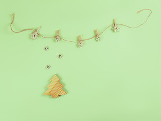 The composition of the handmade wooden fir tree and snowflakes on the rope with the pegs on the green background and place for your text. Christmas or New Year beige and green banner.