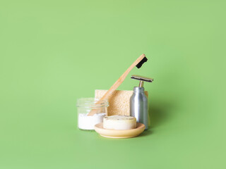 The bamboo toothbrush in glass with toothpowder and the steel multiple-use razor in the bottle, natural round soap and the natural wash gourd against the green background. Zero waste bathing concept.