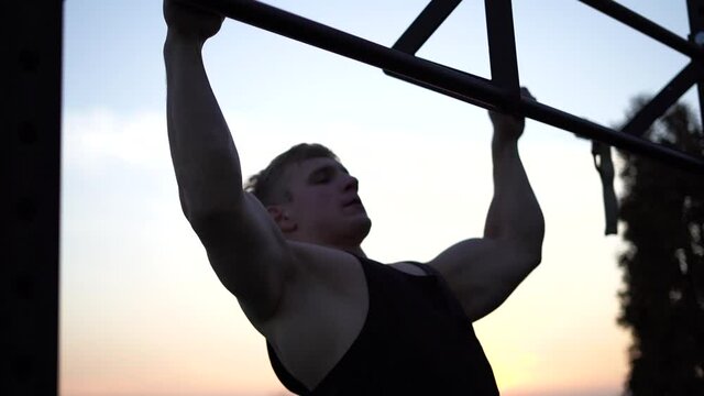 Muscular man doing pullups on sunset sky background. Calisthenics, healthy lifestyle and workout concept 