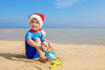 Fototapeta na wymiar smiling child boy in santa hat playing with toys for sand