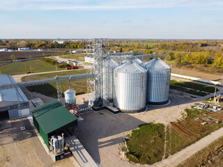 Fototapeta na wymiar Aerial view of granaries. Grain storage and processing plant in countryside. Chrome colored granaries and buildings. Grain storage bins and other agricultural facilities in rural area