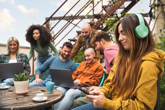 Multiracial group of students working together using digital devices such as laptops and smartphones in the campus terrace, co-working outdoors together