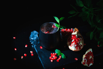 Red cocktail with cold vodka and pomegranate juice, ice cubes and rosemary, bar tools, blue black bar counter background, copy space, selective focus